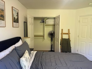 Un dormitorio con una cama, un ventilador, una escalera de madera y un armario con perchero.
