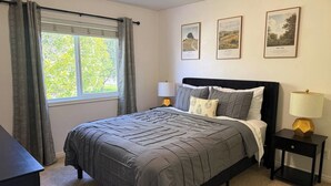 A bedroom with a bed, a nightstand, a lamp, and a window with curtains. There are three framed pictures on the wall. - The Travelers Nest | BYUI, Island Park, & Targhee (Rexburg)