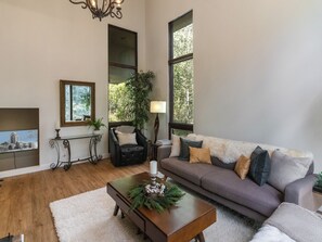 Ein Wohnzimmer mit einer Couch, einem Couchtisch mit Kerze, einer Lampe und einem großen Fenster mit Blick auf Bäume.