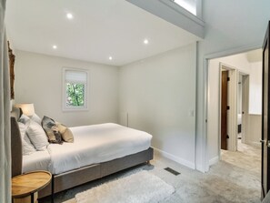 Ein Schlafzimmer mit Bett, Nachttisch, Fenster und einem Flur, der in einen weiteren Raum führt.