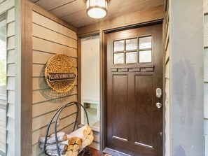 Eine Holztür mit Fensterglas, ein Korb mit Brennholz und ein Schild an der Wand.