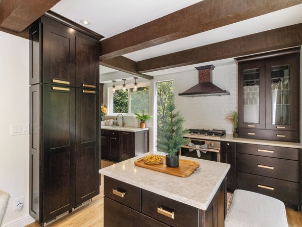 A modern kitchen with dark cabinetry, a marble countertop, and a central island.