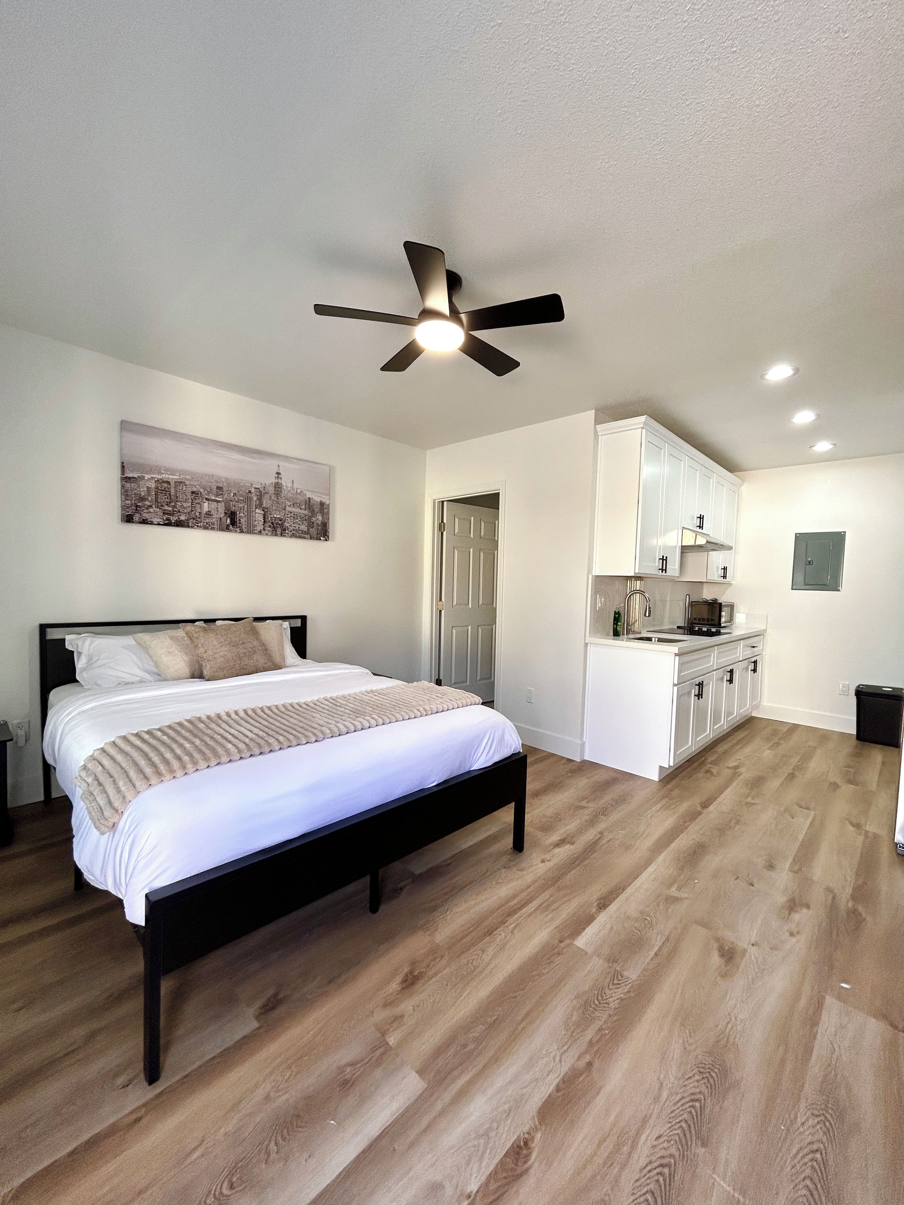 Une chambre à coucher avec un lit, un ventilateur de plafond et un tableau représentant un paysage urbain accroché au mur.