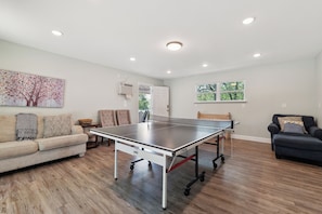 A spacious living room with a ping pong table, a sofa, a chair, and a painting on the wall. - White Oak Retreat! 17 mins to Silos! (Waco)