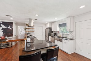 A modern kitchen with a central island, stainless steel appliances, and white cabinetry. - White Oak Retreat! 17 mins to Silos! (Waco)