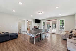 A spacious living room with a ping pong table, a sofa, and a television mounted on the wall. - White Oak Retreat! 17 mins to Silos! (Waco)