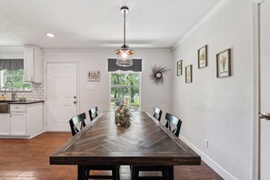 Un coin repas avec une table en bois, des chaises, un luminaire suspendu et des reproductions botaniques encadrées accrochées au mur.