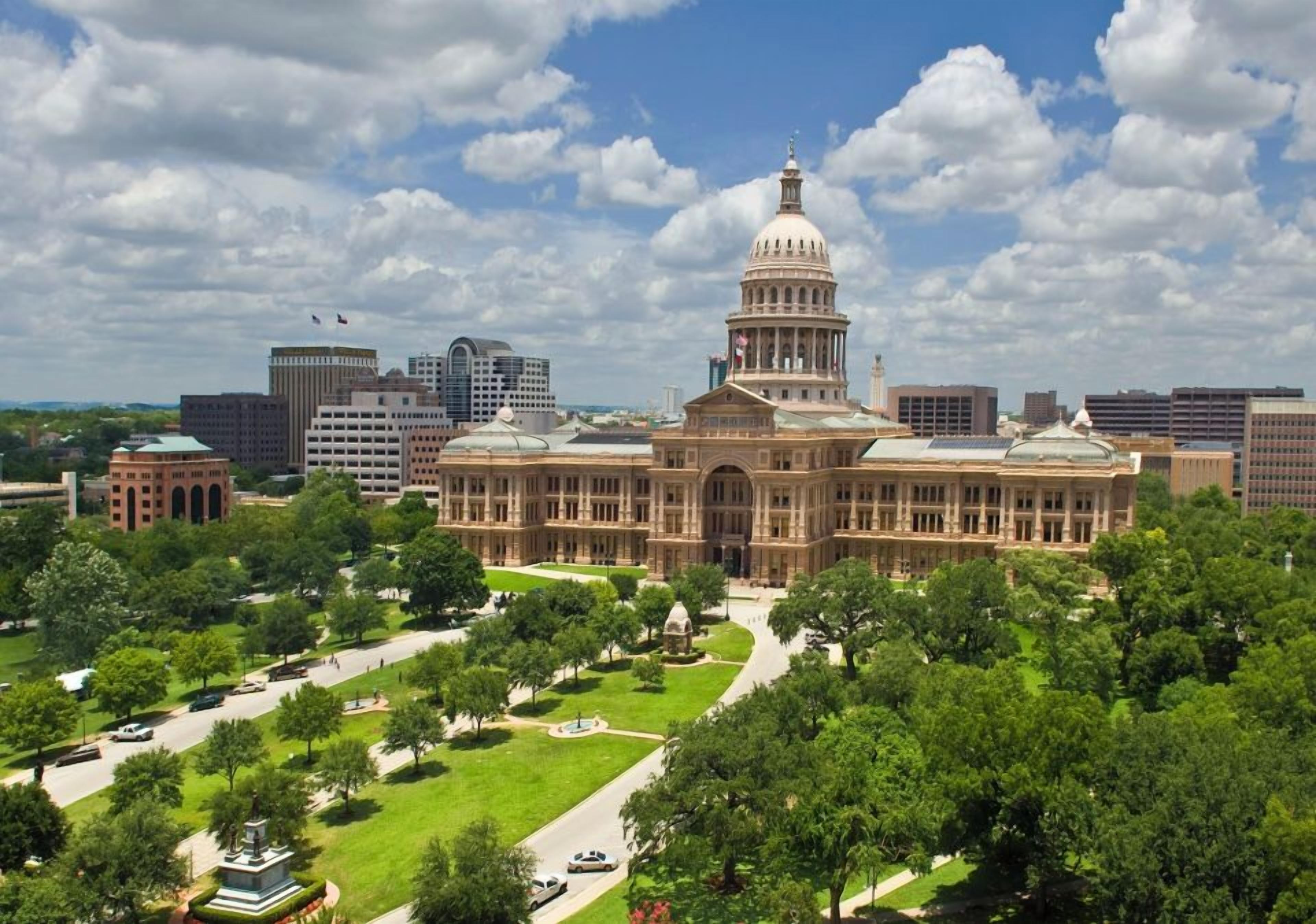 A large, historic building with a prominent dome, surrounded by lush green lawns and trees.