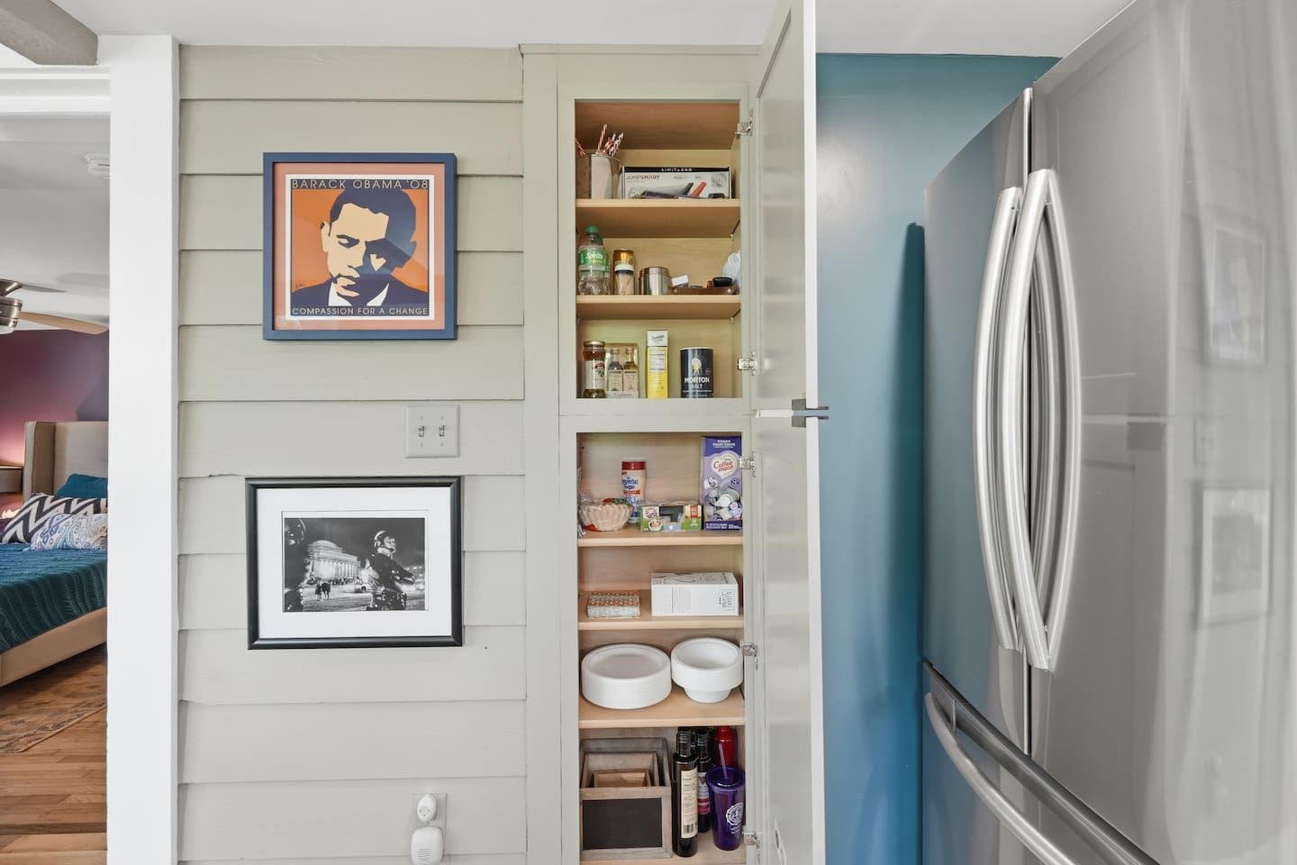 A modern kitchen with a built-in refrigerator, a pantry with various food items, and two framed pictures on the wall.