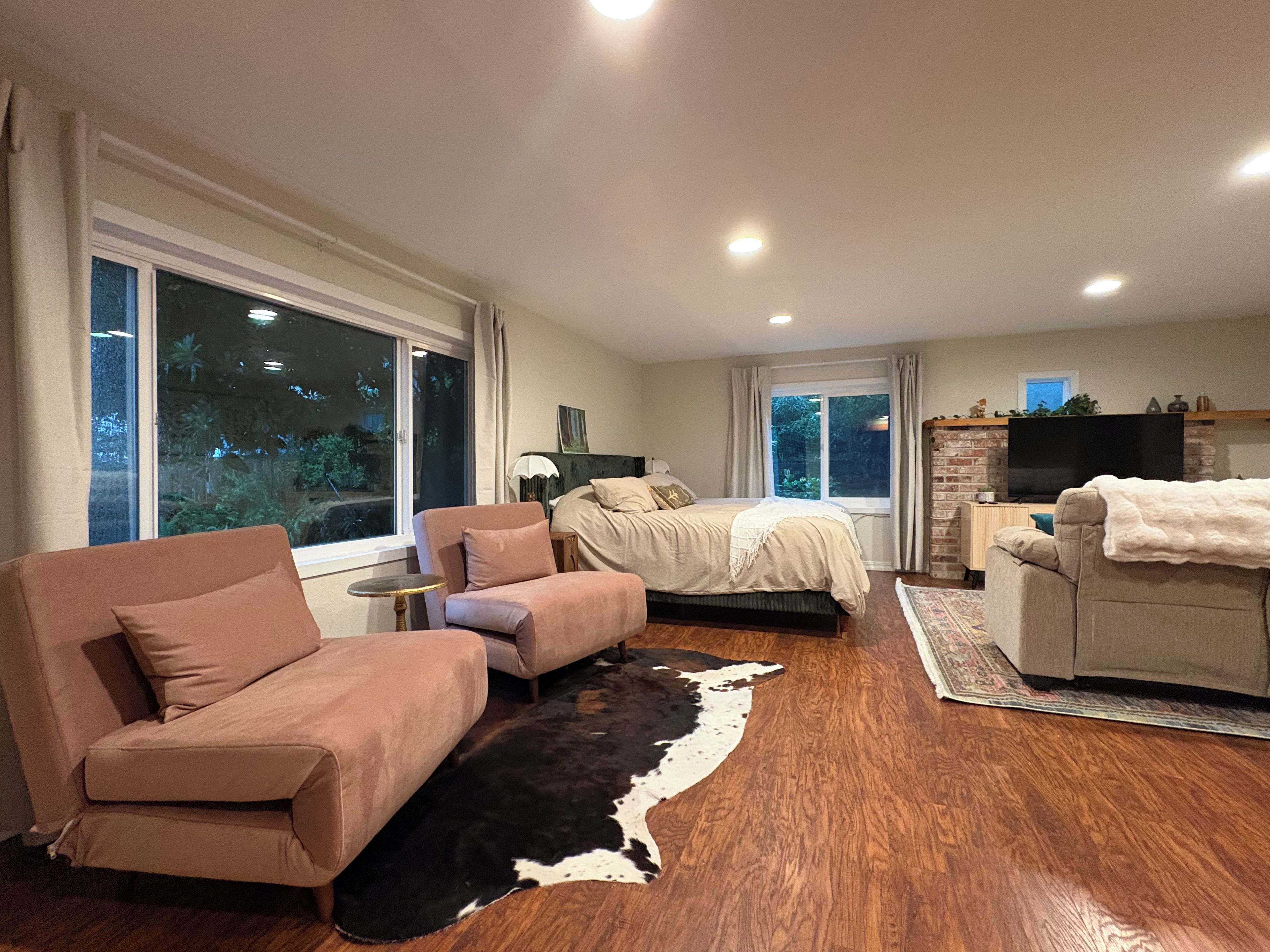 A modern bedroom with a large bed, a sofa, a television, and a fireplace.