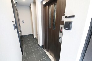 A hallway with a dark wooden elevator door, a number 103 sign, and a keypad on the wall. - Lamarie Haneda 402 (Ota Ku)