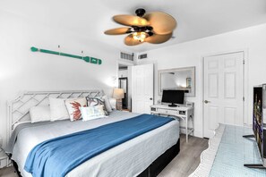 Ein Hotelzimmer mit einem Bett, einem Schreibtisch mit Computer, einem Fernseher und einem Deckenventilator.