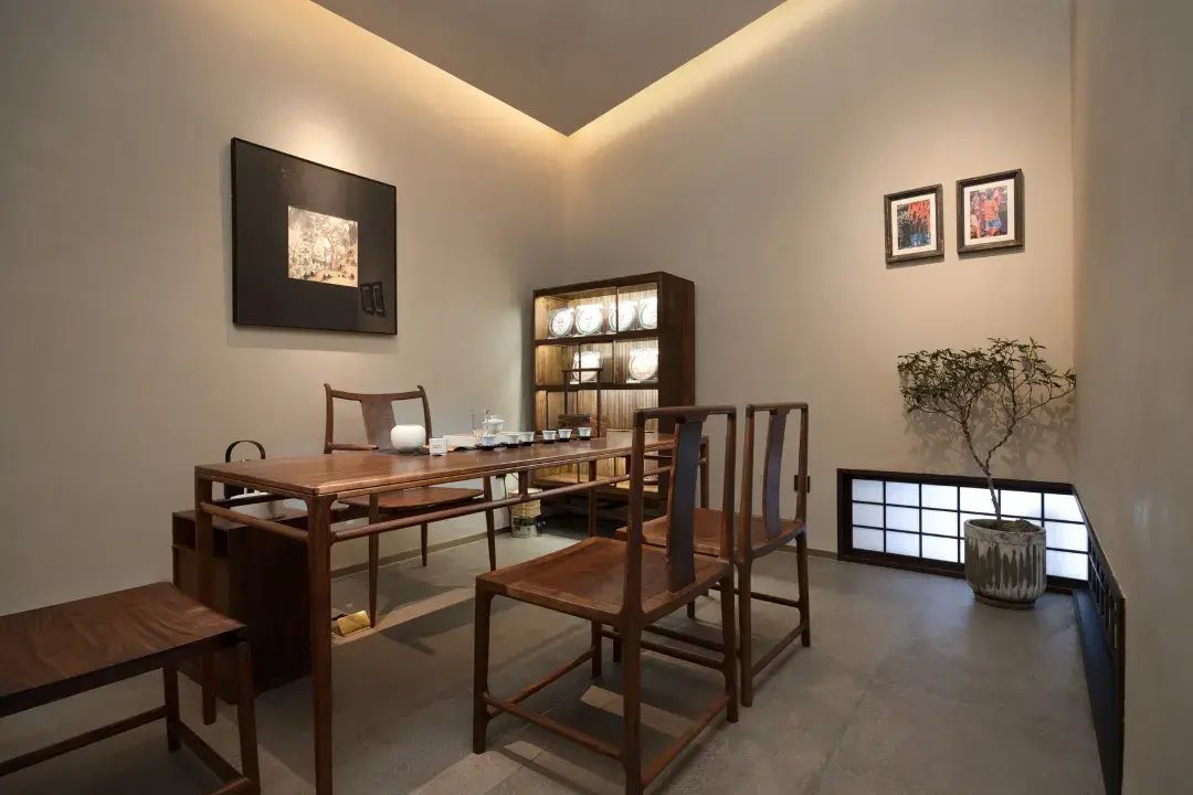 A dining area with a wooden table and chairs, a cabinet with illuminated shelves, and framed artwork on the walls.