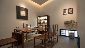 A dining area with a wooden table and chairs, a cabinet with illuminated shelves, and framed artwork on the walls.