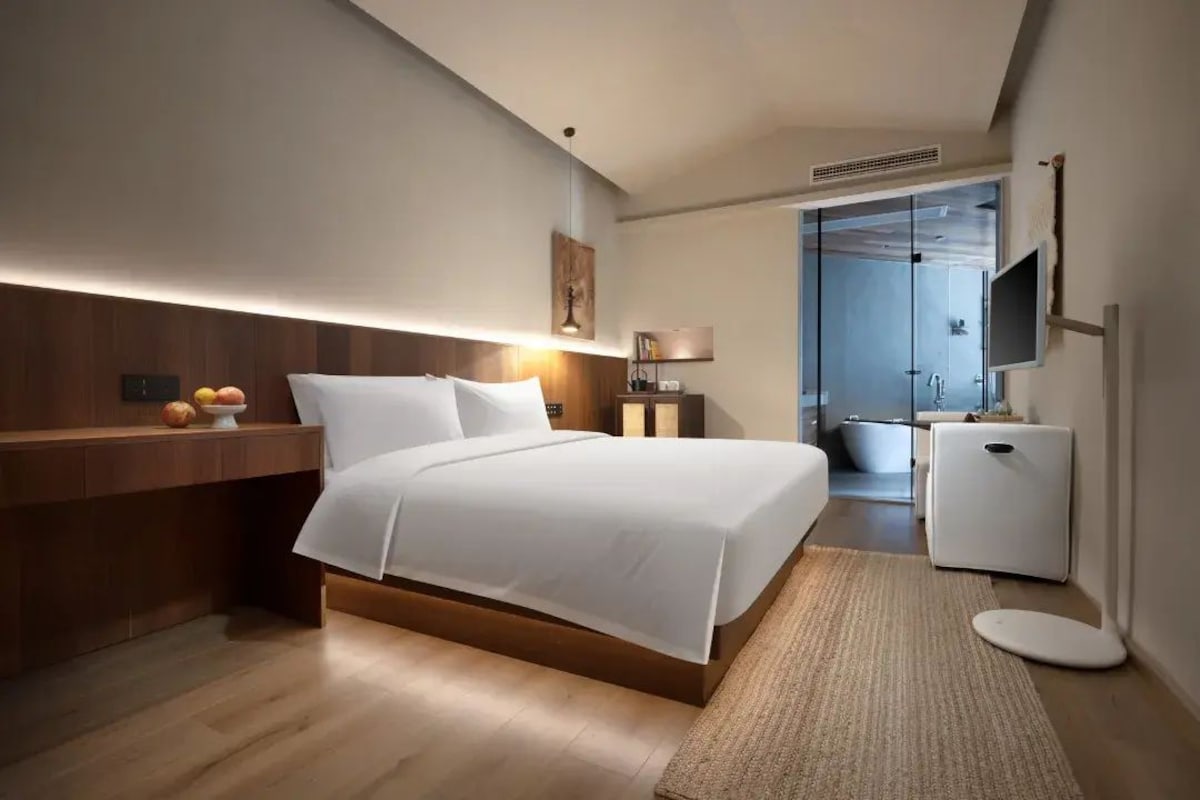 Quarto de hotel moderno com uma cama grande, mesa de cabeceira e uma pequena escrivaninha com uma cadeira.