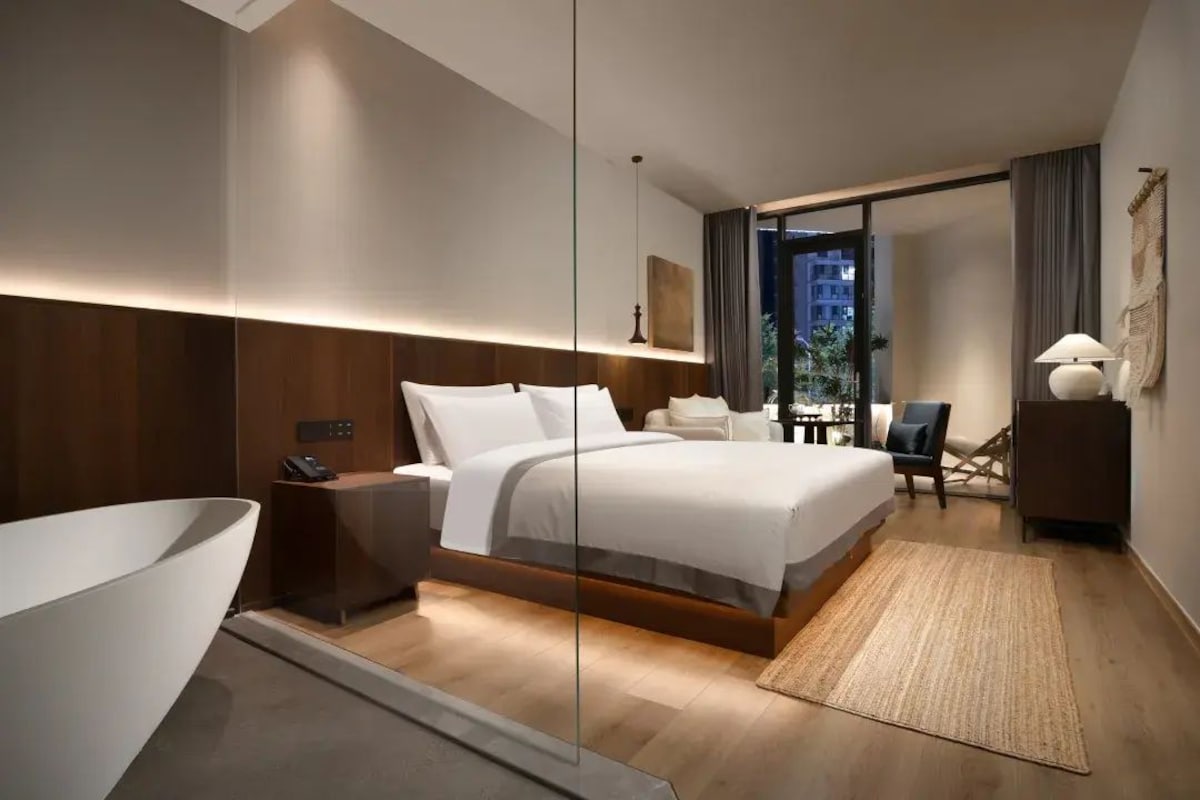 Quarto de hotel moderno com cama grande, mesa de cabeceira e vista para a cidade.