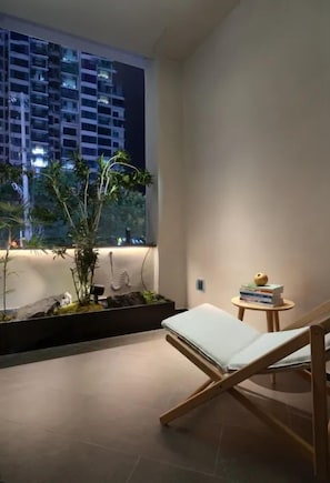A room with a bed, a small table with books, a window with a view of buildings, and a plant arrangement. - Ruke Holiday Homestay Zhangjiajie (Zhangjiajie)