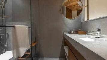 A modern bathroom with a glass shower enclosure, a wooden vanity, and a round mirror.