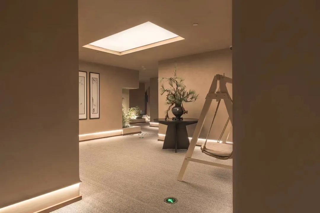 A hotel lobby with a high ceiling, a skylight, a central table with a plant, and a chair.