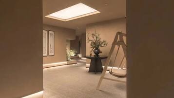 A hotel lobby with a high ceiling, a skylight, a central table with a plant, and a chair.