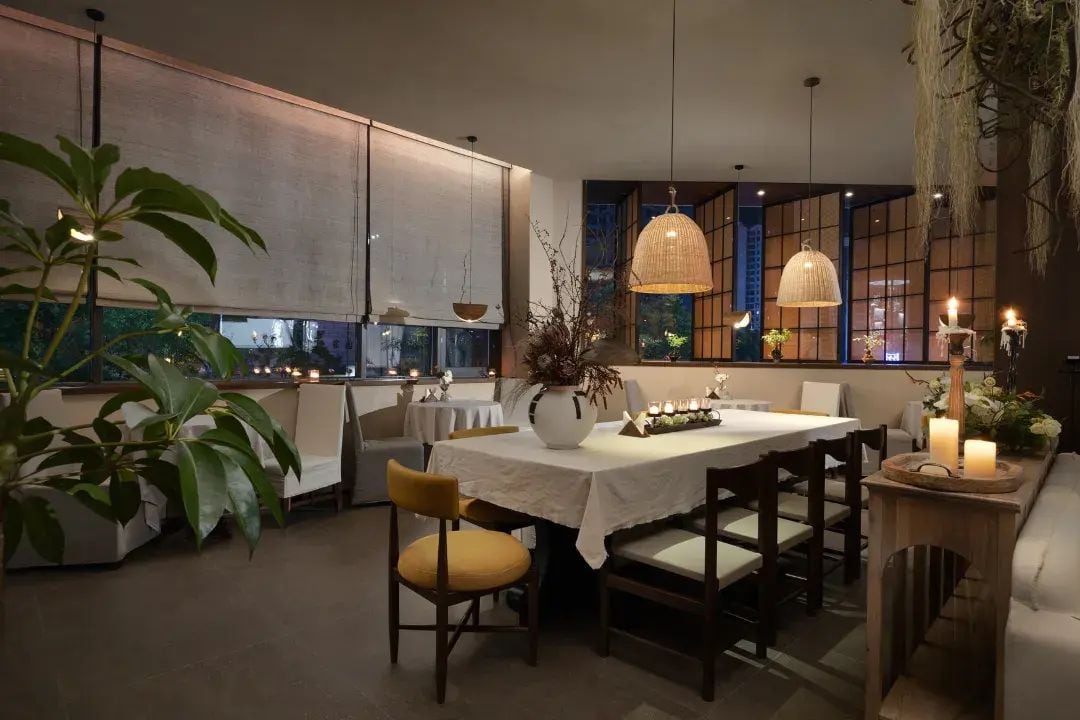 Un comedor con una mesa dispuesta para dos personas, rodeada de sillas, con un florero y velas sobre la mesa.