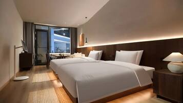 Una habitación de hotel moderna con una cama grande, mesitas de noche, un escritorio y vistas a través de un ventanal.