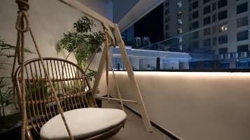 A hanging chair with ropes, a potted plant, and a view of a building at night.