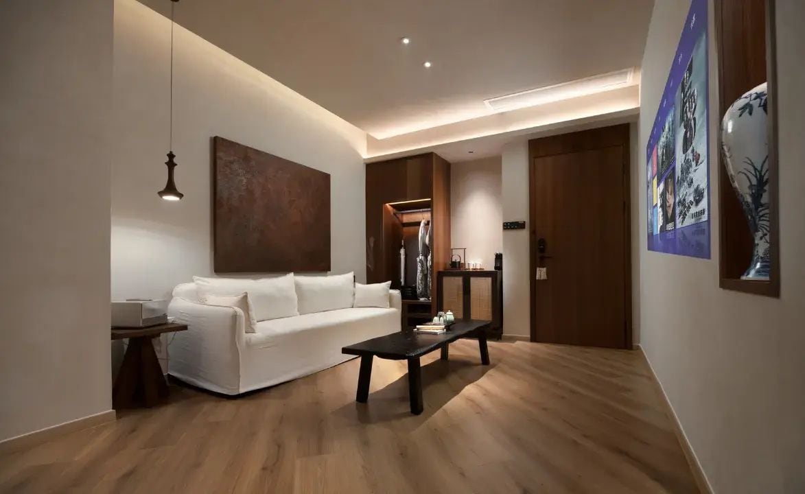 Uma sala de estar moderna com um sofá branco, uma mesa de centro preta e uma luminária pendente.