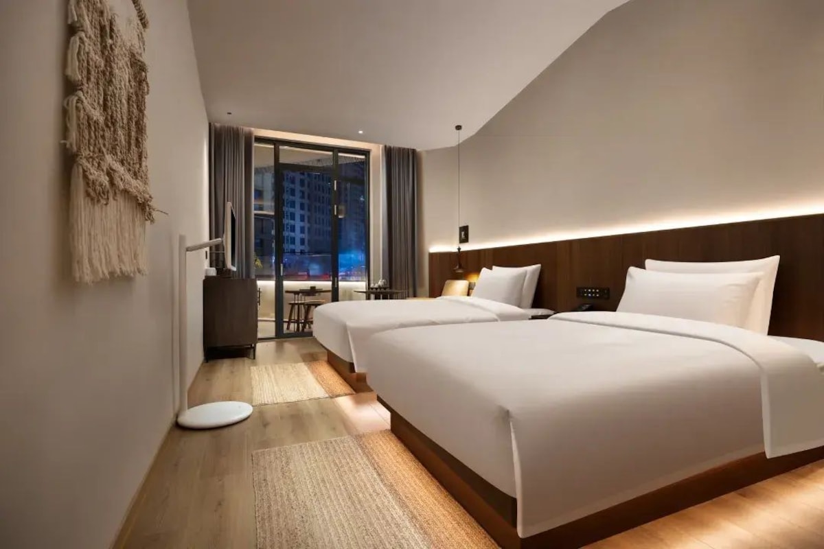 Quarto de hotel moderno com duas camas, vista para a cidade e um pequeno espaço de estar.