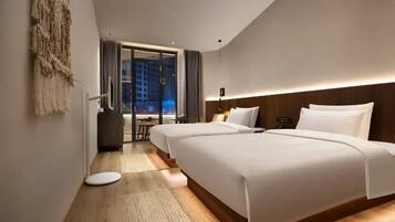 A modern hotel room with two beds, a view of the city, and a small seating area.