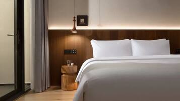Quarto de hotel com cama, mesa de cabeceira com abajur, painel de cabeceira de madeira e quadro pendurado na parede.