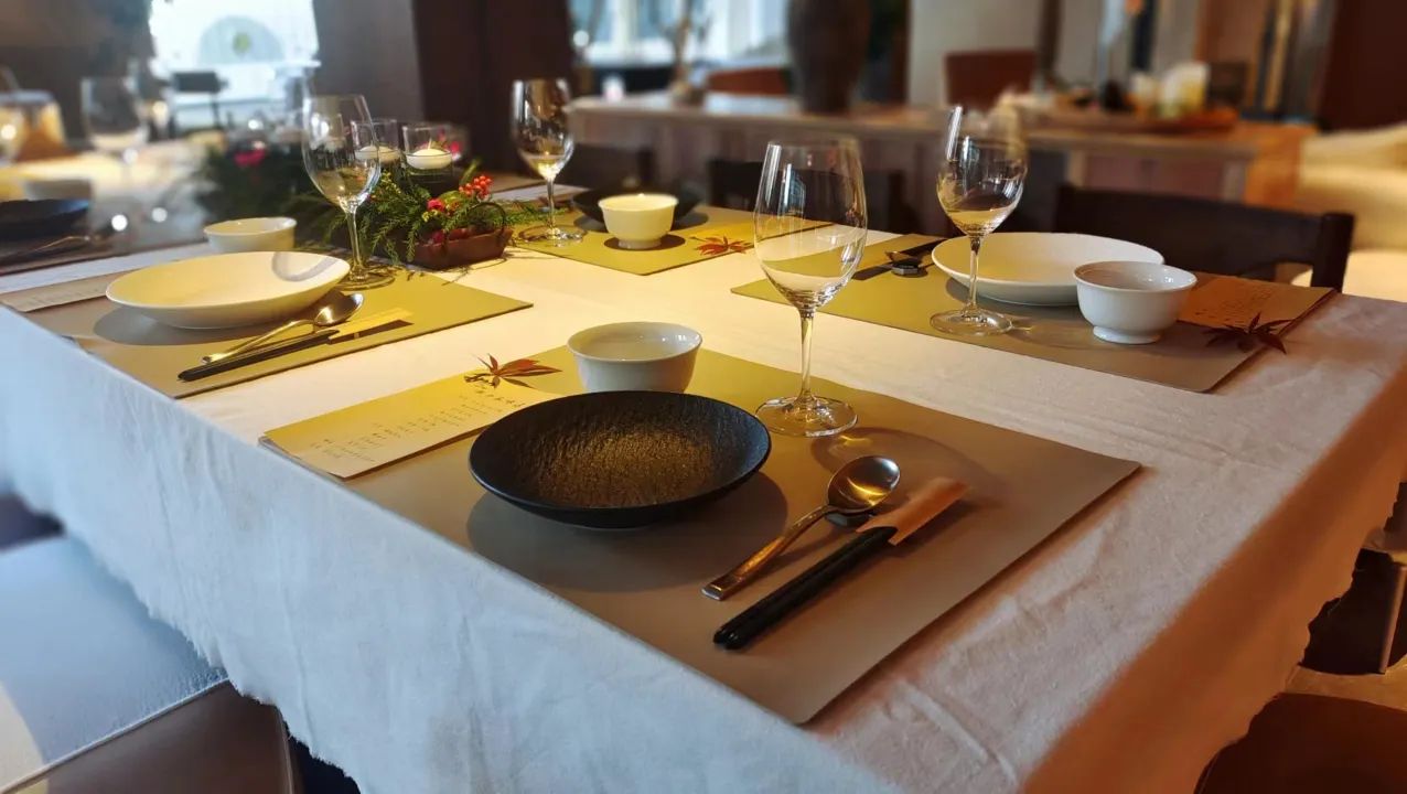Mesa de jantar posta com pratos, talheres, copos e uma tigela, indicando uma refeição preparada.
