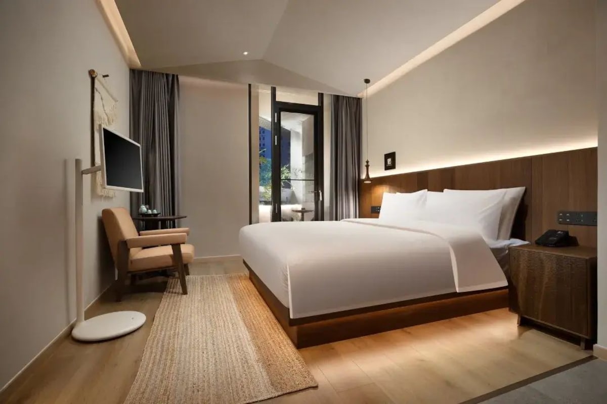 Quarto de hotel moderno com uma cama grande, uma escrivaninha, uma cadeira, uma televisão e vista para o exterior.