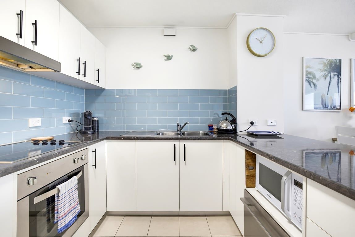 A kitchen with white cabinets, a black countertop, a microwave, and a clock on the wall.