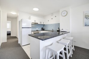 A modern kitchen with a central island, white cabinetry, and a blue backsplash. - 10 Coral Seas - Beachside Escape in the Heart of Cotton Tree (Maroochydore)