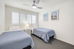 A hotel room with two beds, a ceiling fan, a nightstand with a lamp, and two framed pictures on the wall. - 10 Coral Seas - Beachside Escape in the Heart of Cotton Tree (Maroochydore)