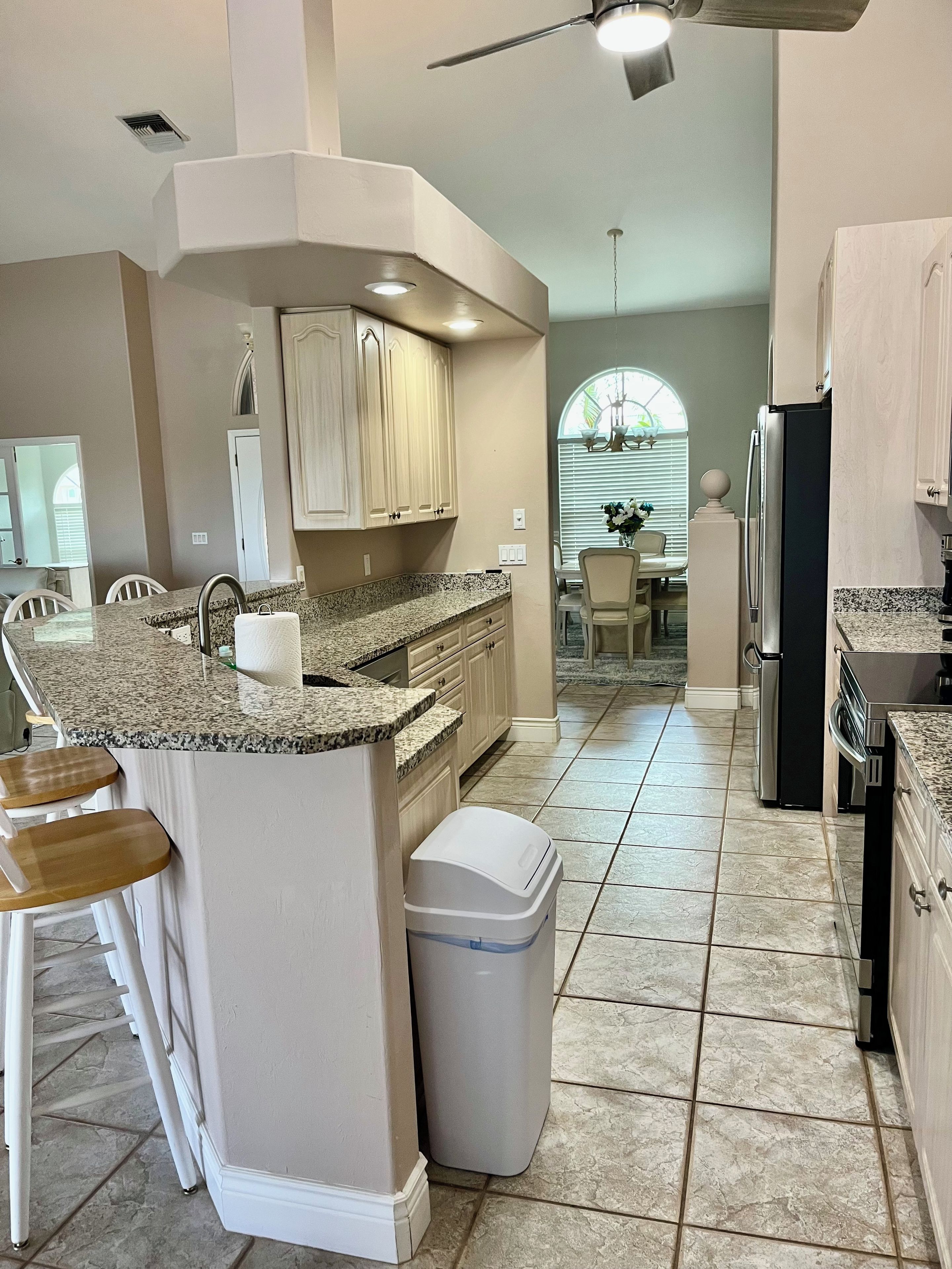 A kitchen with a granite countertop, white cabinets, a stainless steel refrigerator, and a trash can.