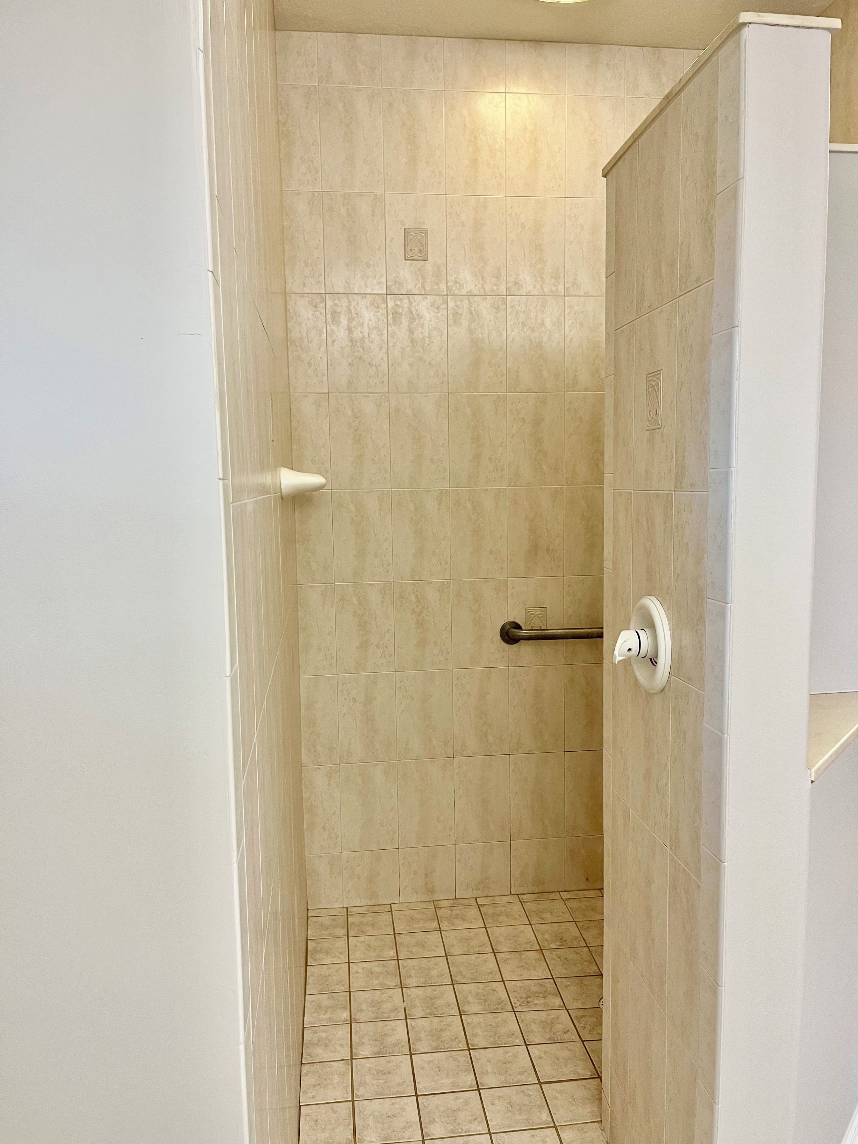 Un baño con baldosas color crema, una puerta blanca y un toallero blanco.