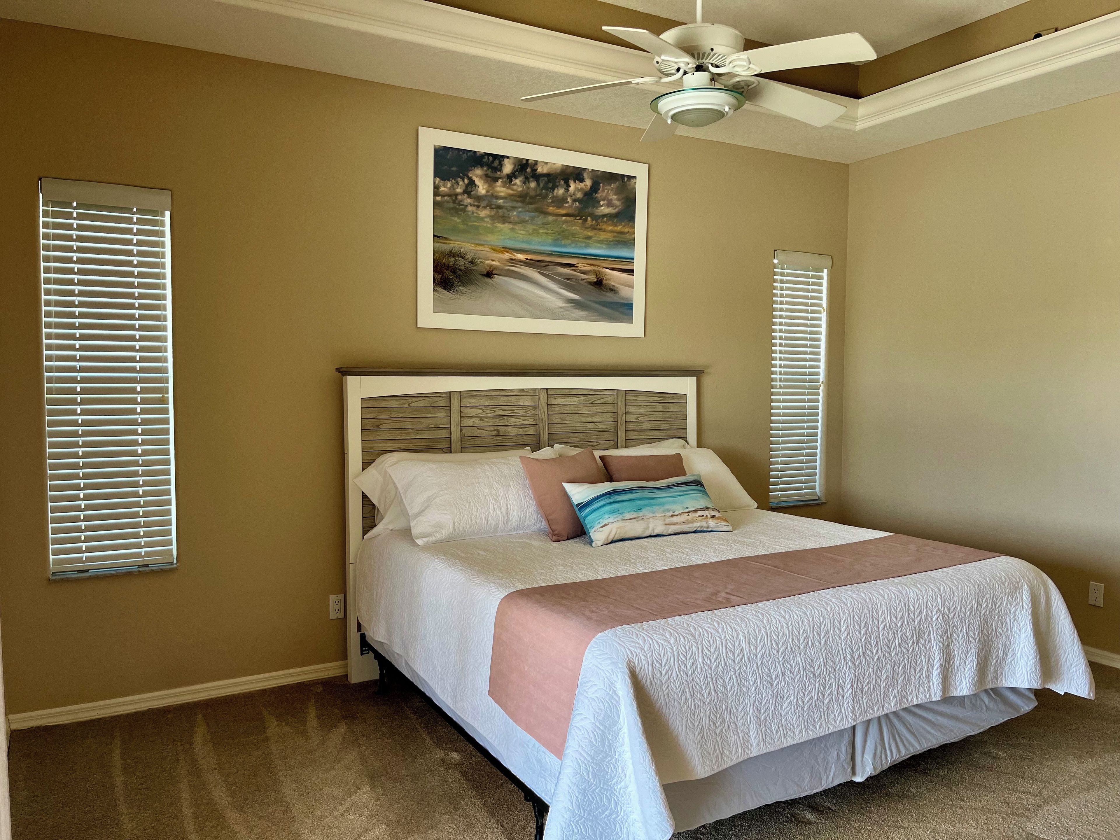 A bedroom with a bed, a ceiling fan, and a painting on the wall.