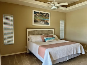 Une chambre à coucher avec un lit, un ventilateur de plafond et un tableau accroché au mur.