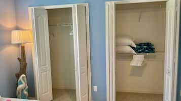 Een slaapkamer met een bed, nachtkastje, lamp en een inbouwkast met hangende kleding.