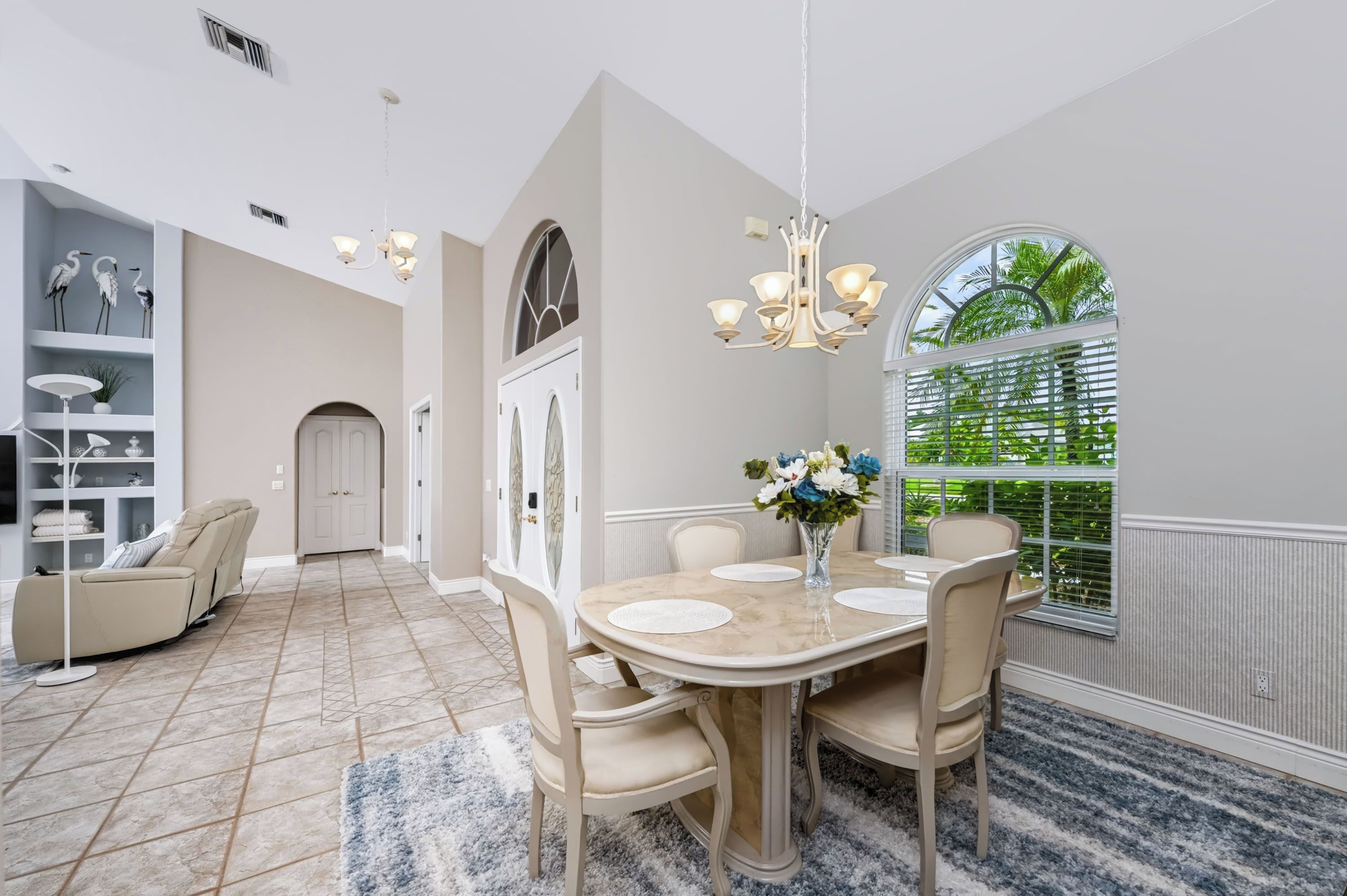 A dining area with a marble table, beige chairs, and a chandelier.