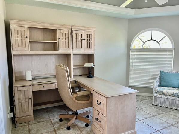A room with a wooden desk, chair, and shelving unit.