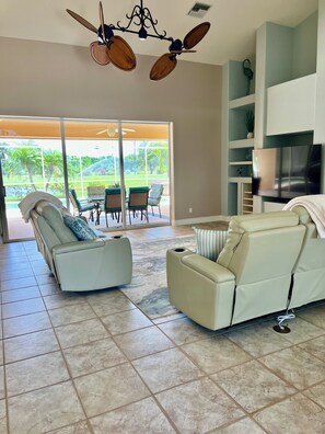 A spacious living area with a sliding glass door leading to a patio, a ceiling fan, a flat-screen TV, and a sofa.