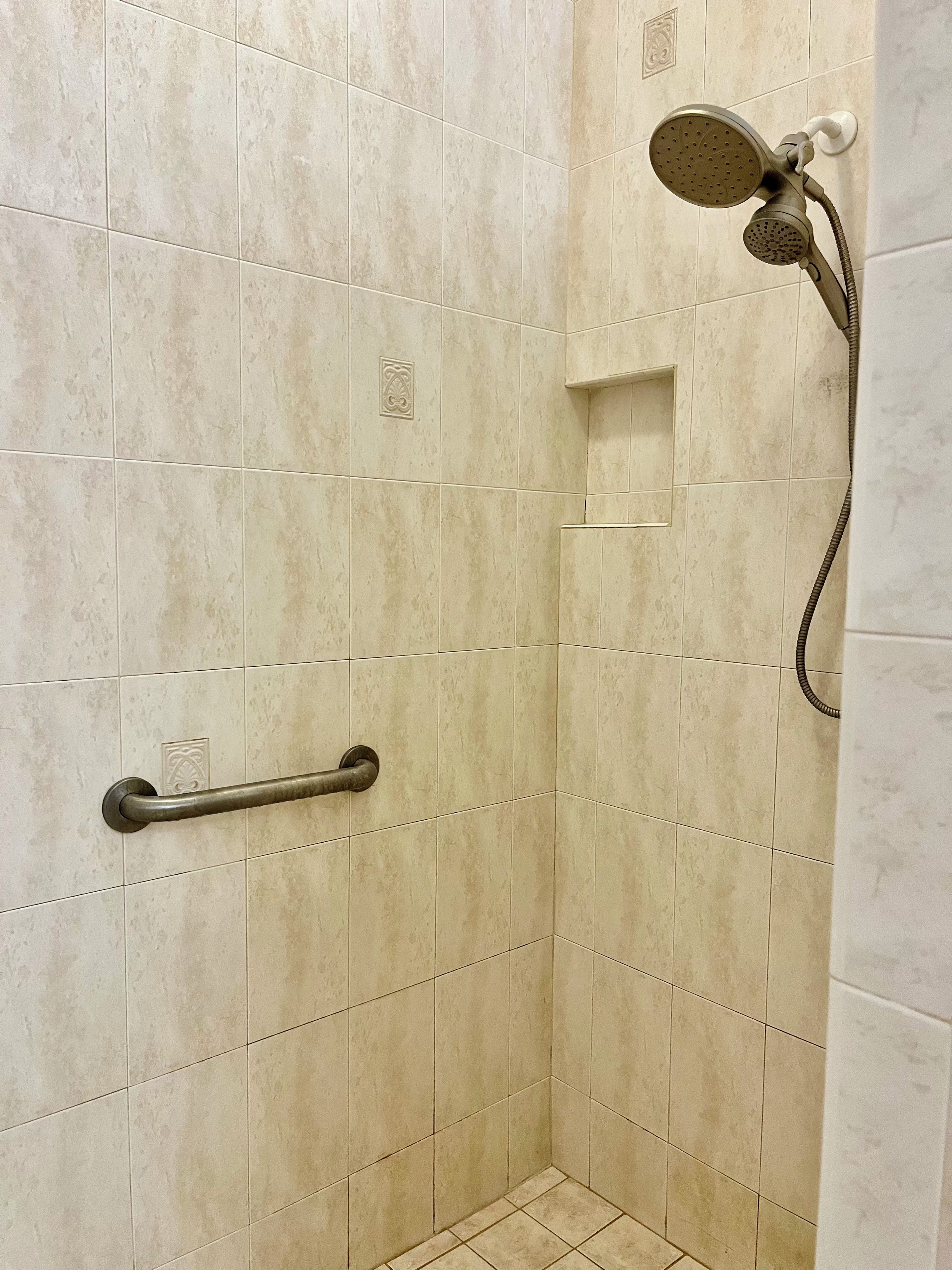 A shower area with beige tiles, a handheld showerhead, and a grab bar.