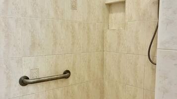 A shower area with beige tiles, a handheld showerhead, and a grab bar.