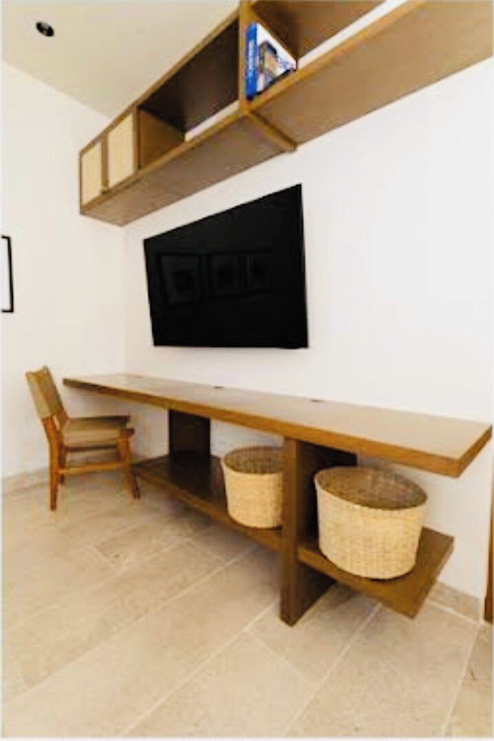 Une pièce avec un téléviseur à écran plat fixé au mur, un bureau en bois, une chaise et deux paniers en osier posés sur le sol.