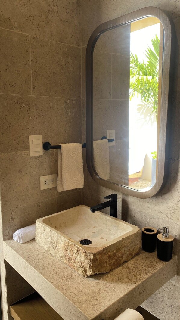 Un bagno con un lavandino in pietra, uno specchio e un portascopevoli.