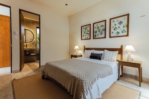 Una camera d'albergo con un letto grande, due comodini con lampade, una testiera in legno e tre opere d'arte appese alle pareti.