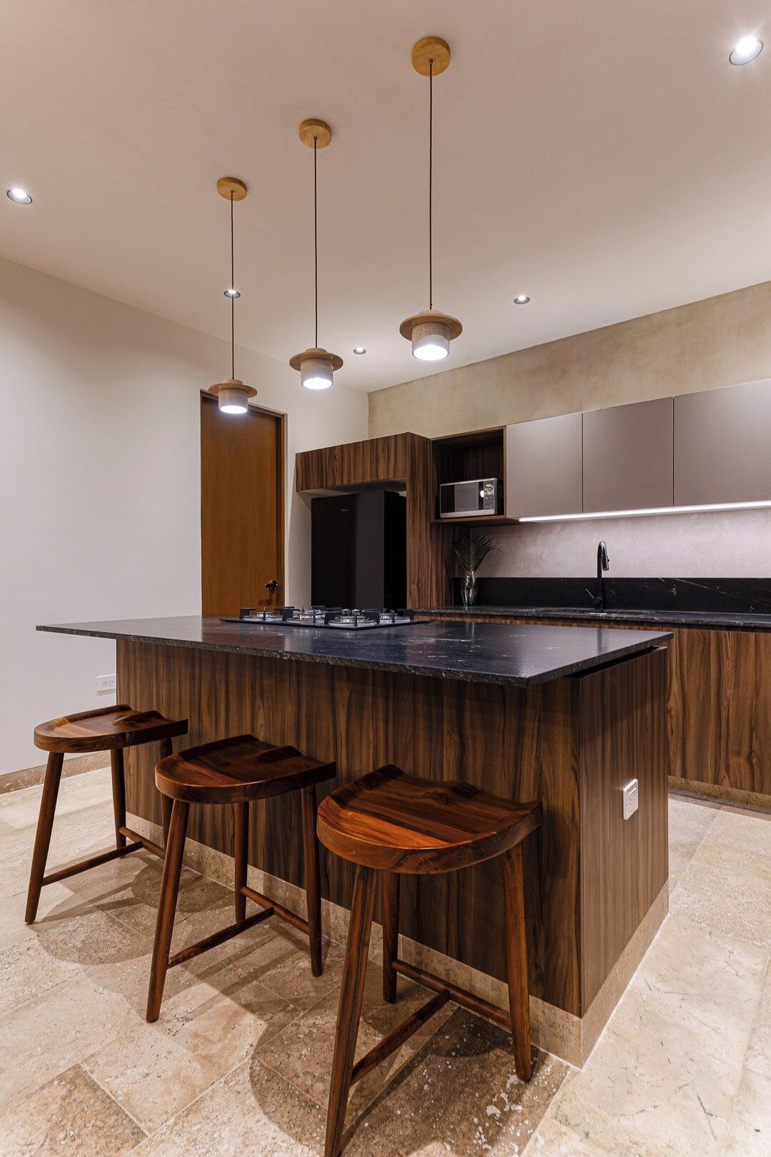 A modern kitchen with a central island, bar stools, pendant lighting, and built-in appliances.
